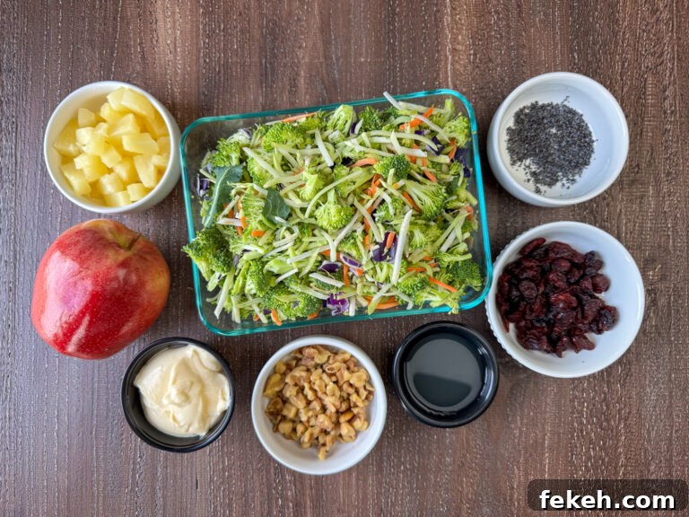 Creamy Broccoli Slaw with Crunchy Apples and Almonds 4 Ingredients to make broccoli slaw salad are pineapple tidbits and juice, broccoli slaw, poppy seeds, dried cranberries, walnuts, light mayo and an apple on a wooden counter top.