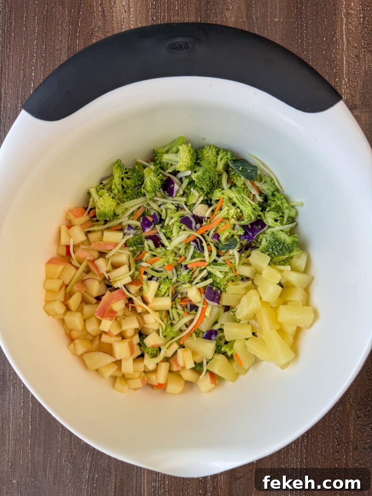 Creamy Broccoli Slaw with Crunchy Apples and Almonds 5 White mixing bowl with a bag of broccoli slaw, diced apples and pineapple tidbits.