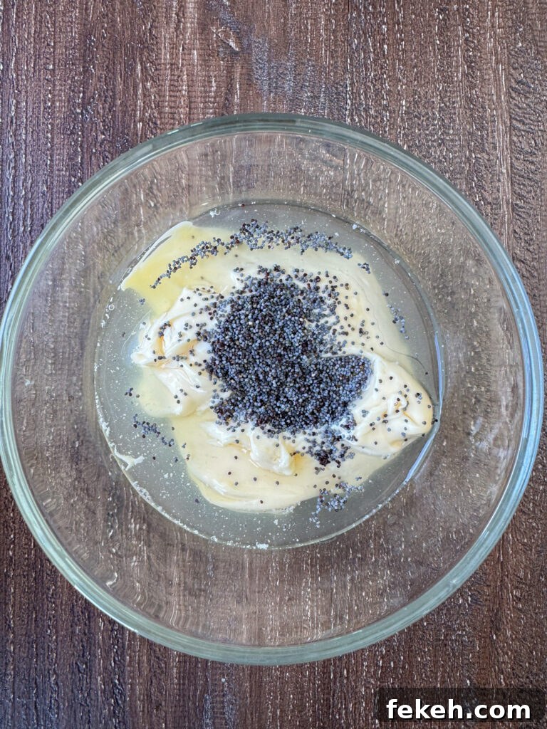 Creamy Broccoli Slaw with Crunchy Apples and Almonds 7 Light mayo in a glass dish with pineapple juice and poppy seeds poured on top.