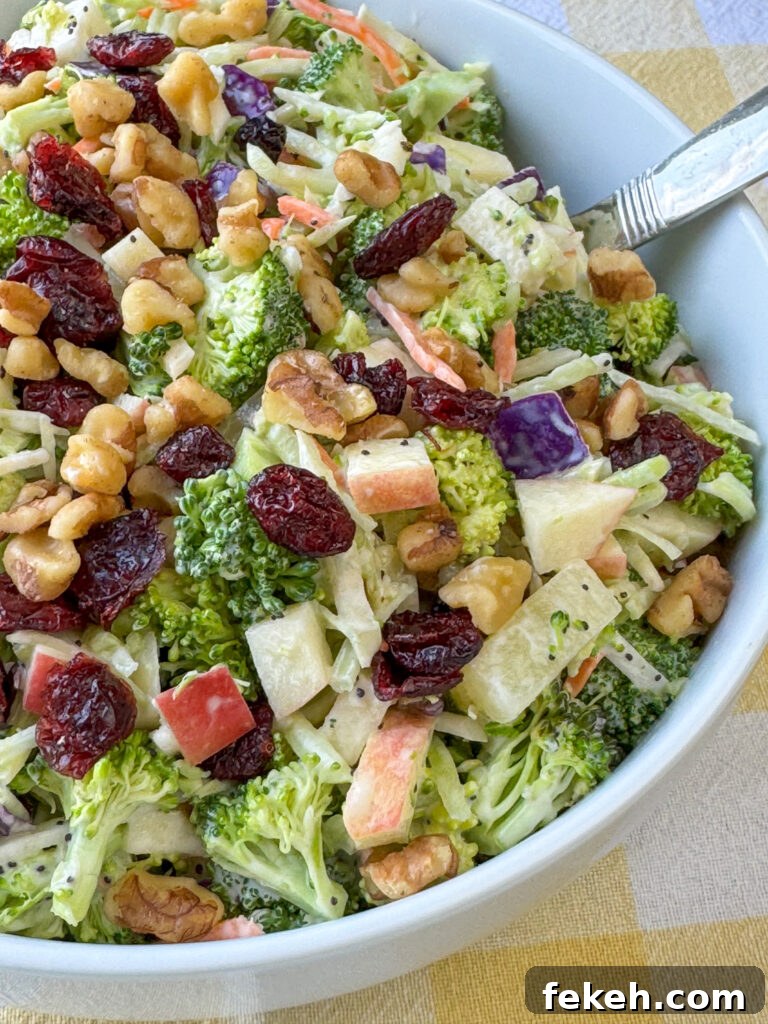Creamy Broccoli Slaw with Crunchy Apples and Almonds 9 Close up of creamy broccoli slaw garnished with dried cranberries and walnuts in a white bowl.