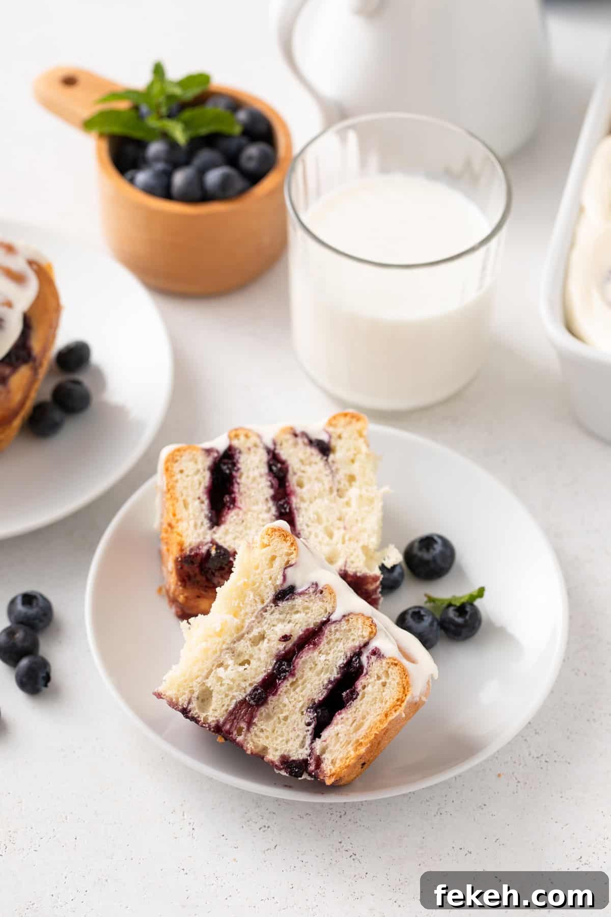 Blueberry sweet roll cut in half on a white plate in front of a glass of milk.