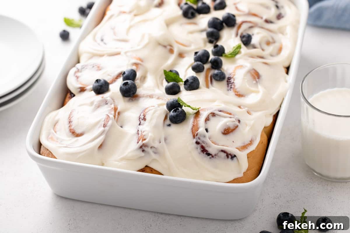 Blueberry sweet rolls topped with cream cheese frosting and garnished with fresh blueberries.