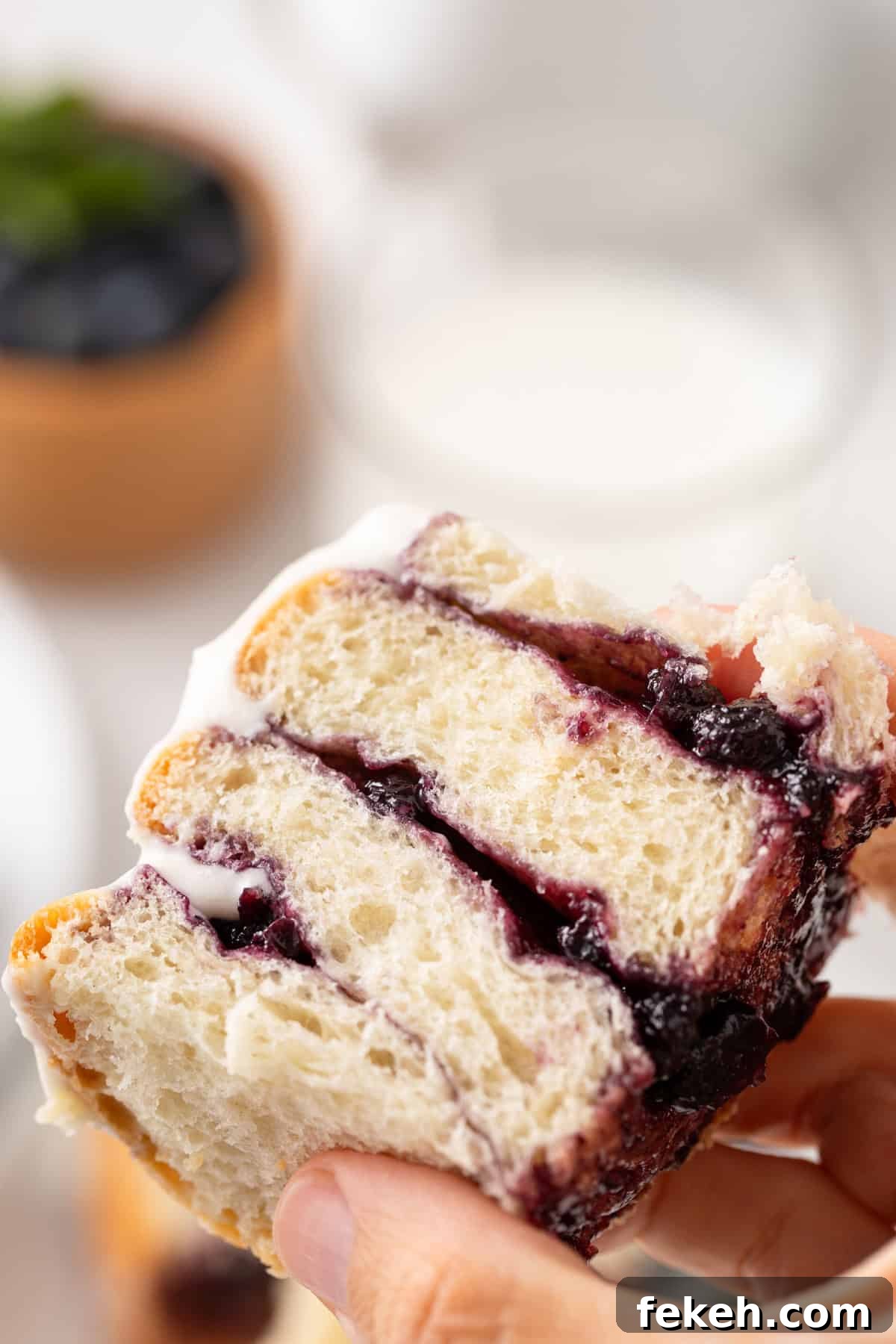Hand holding up half of a blueberry sweet roll to the camera.