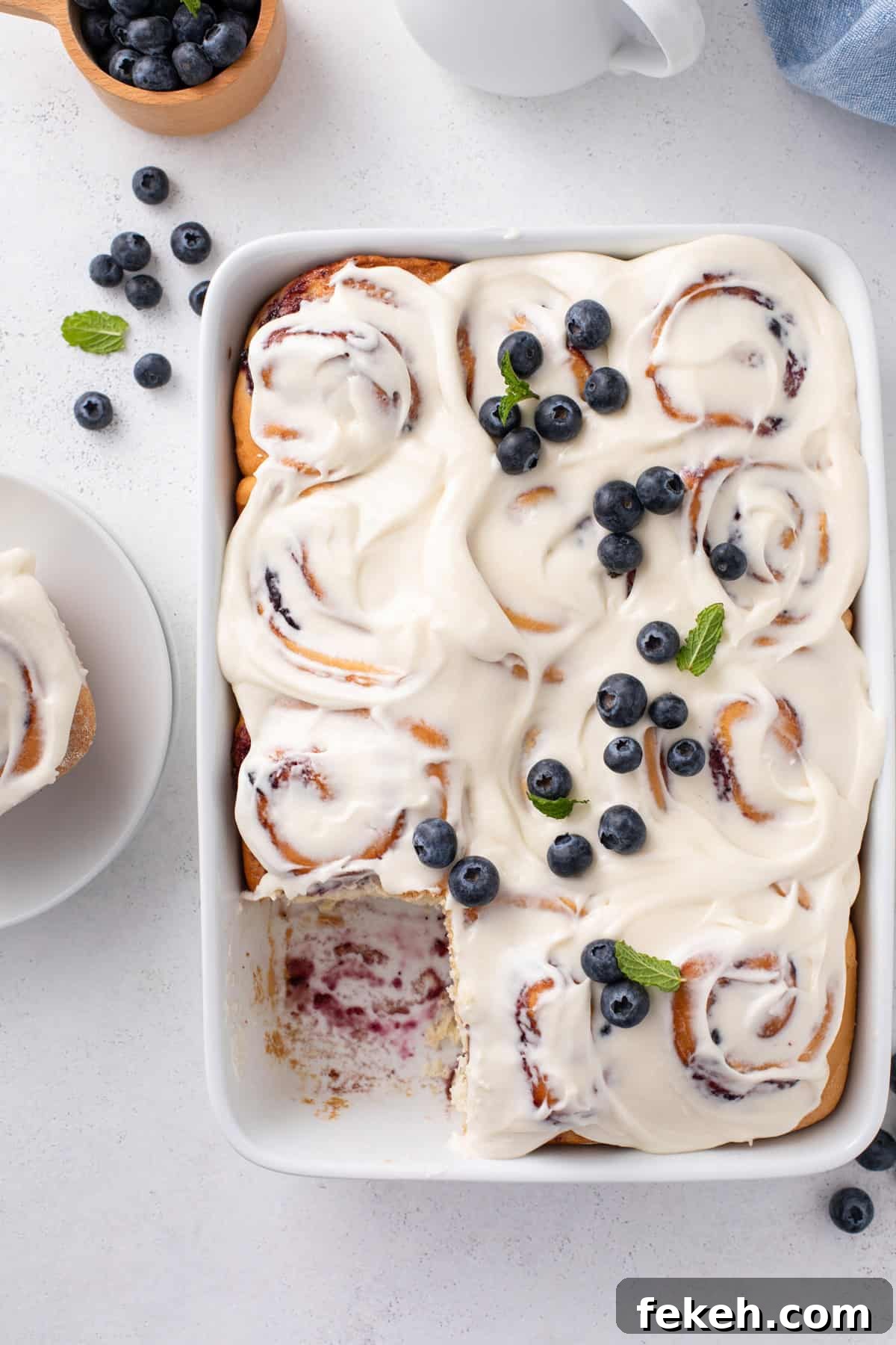 Overhead view of a pan of blueberry sweet rolls with one roll removed from the corner of the pan.
