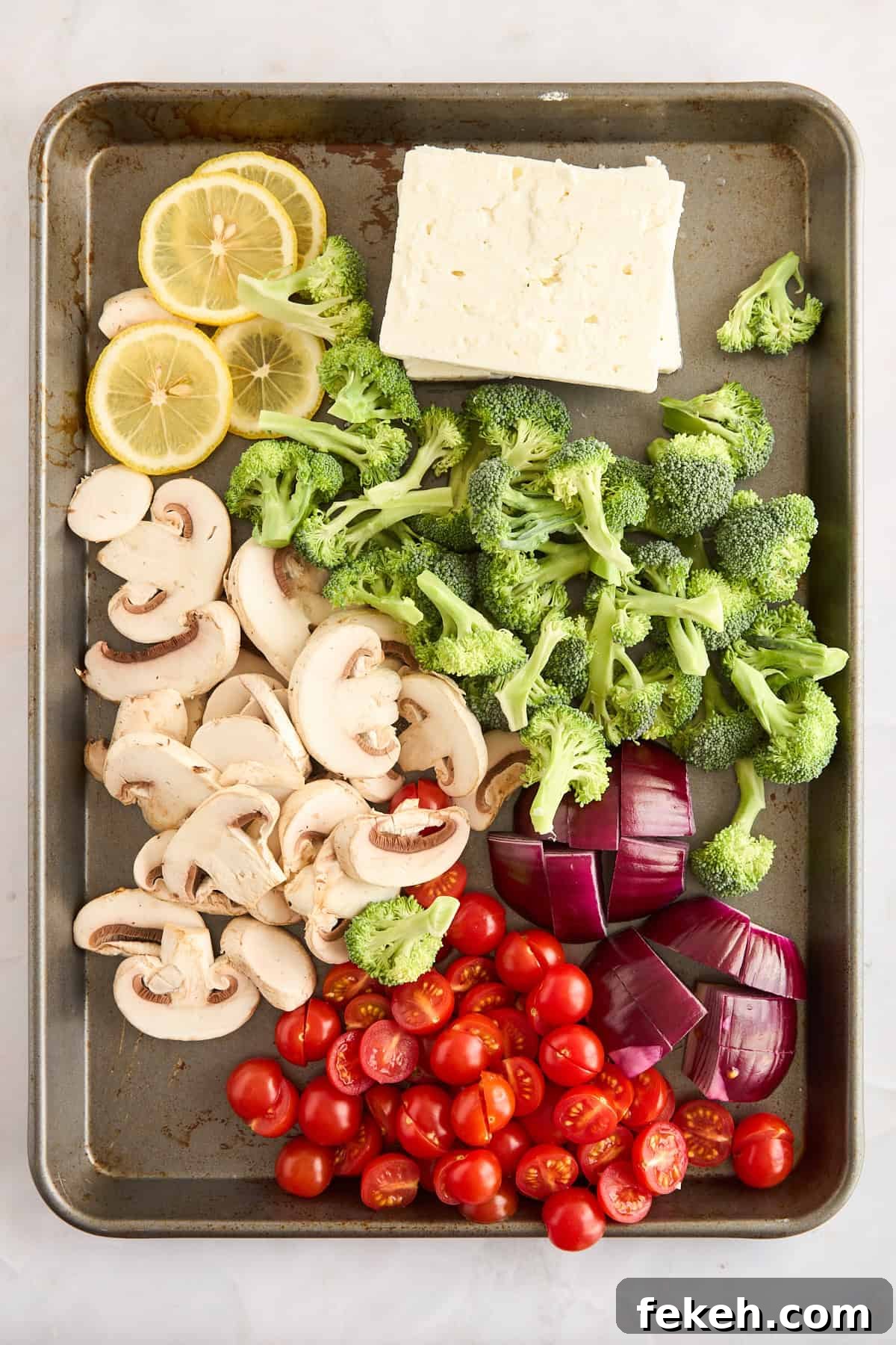 Raw veggies and feta blocks on a sheet pan. 