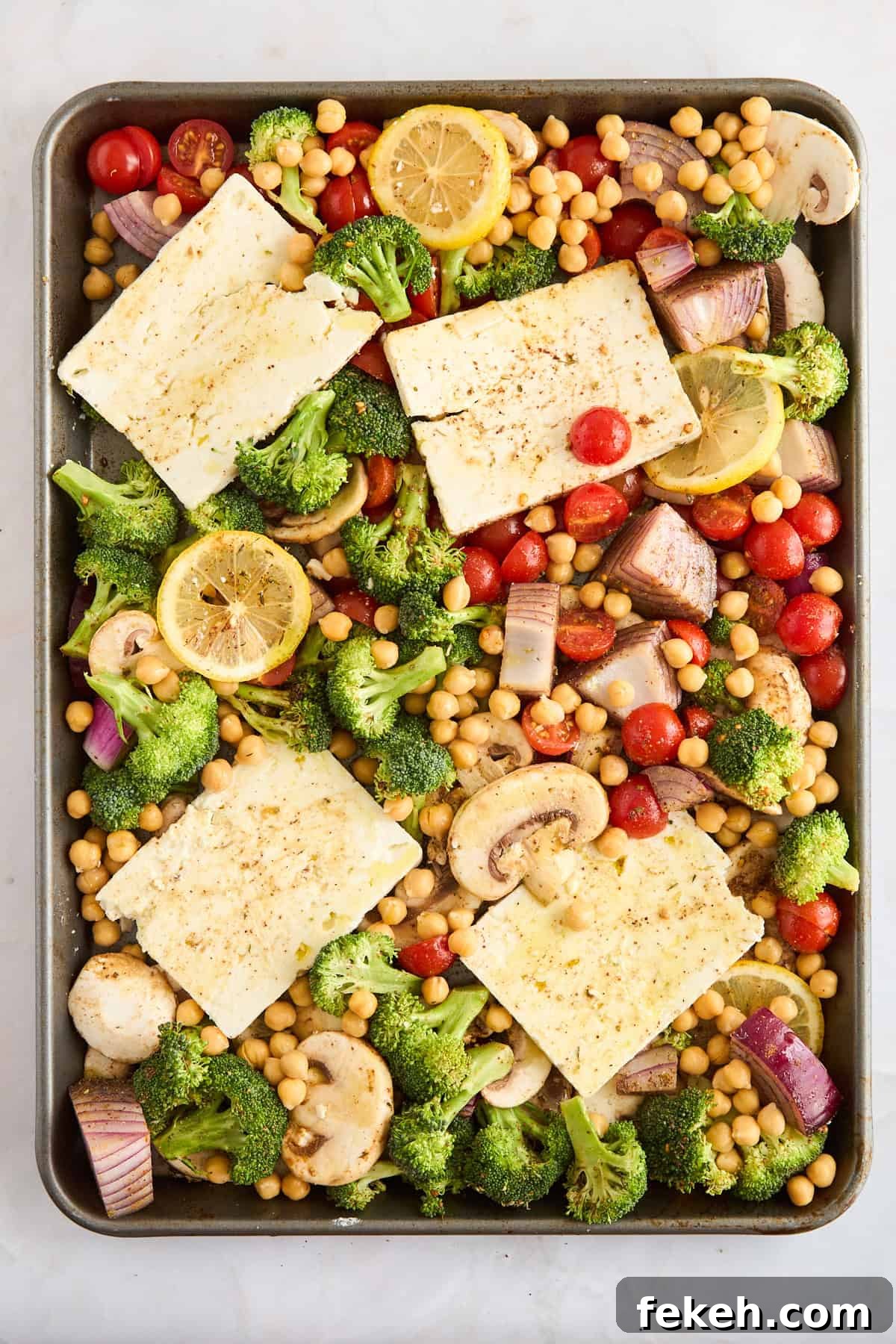 Seasoned raw veggies, feta, and chickpeas on a sheet pan. 