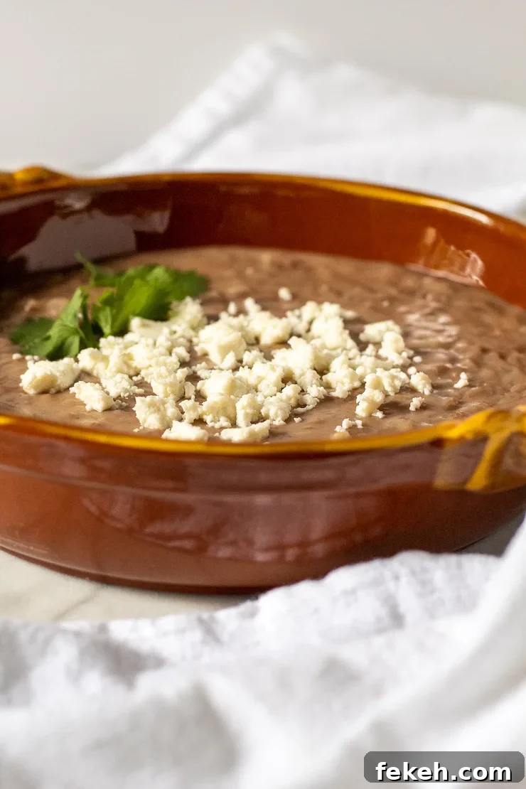 Homestyle Refried Beans Recipe for Creamy, Flavorful Sides 7 Sideview in serving dish with cheese on top.