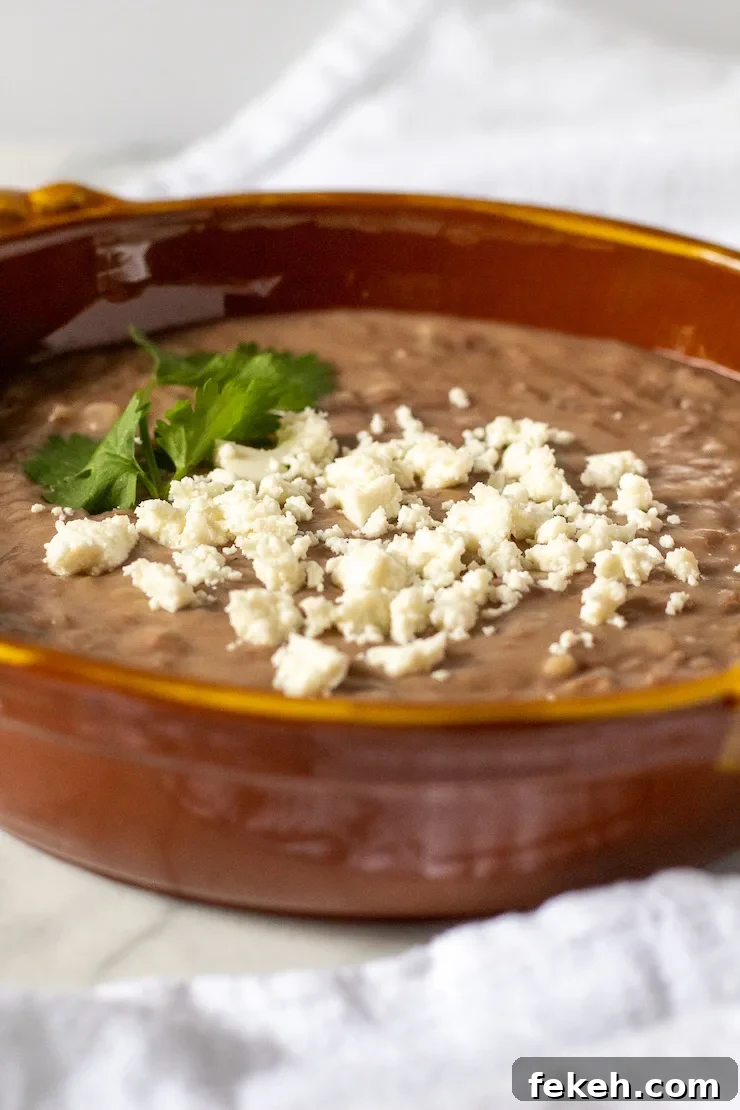 Homestyle Refried Beans Recipe for Creamy, Flavorful Sides 8 Refried beans in serving dish with queso fresco.