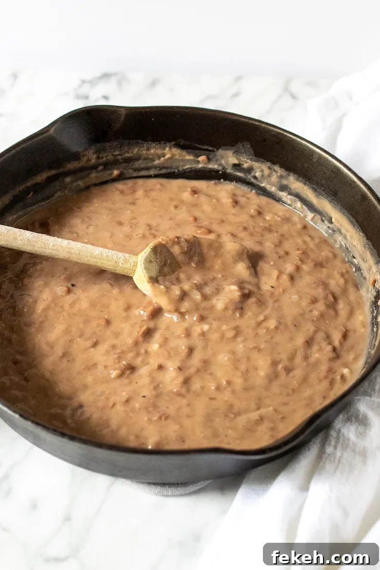 Homestyle Refried Beans Recipe for Creamy, Flavorful Sides 3 Refried beans in cast iron skillet with wooden spoon.