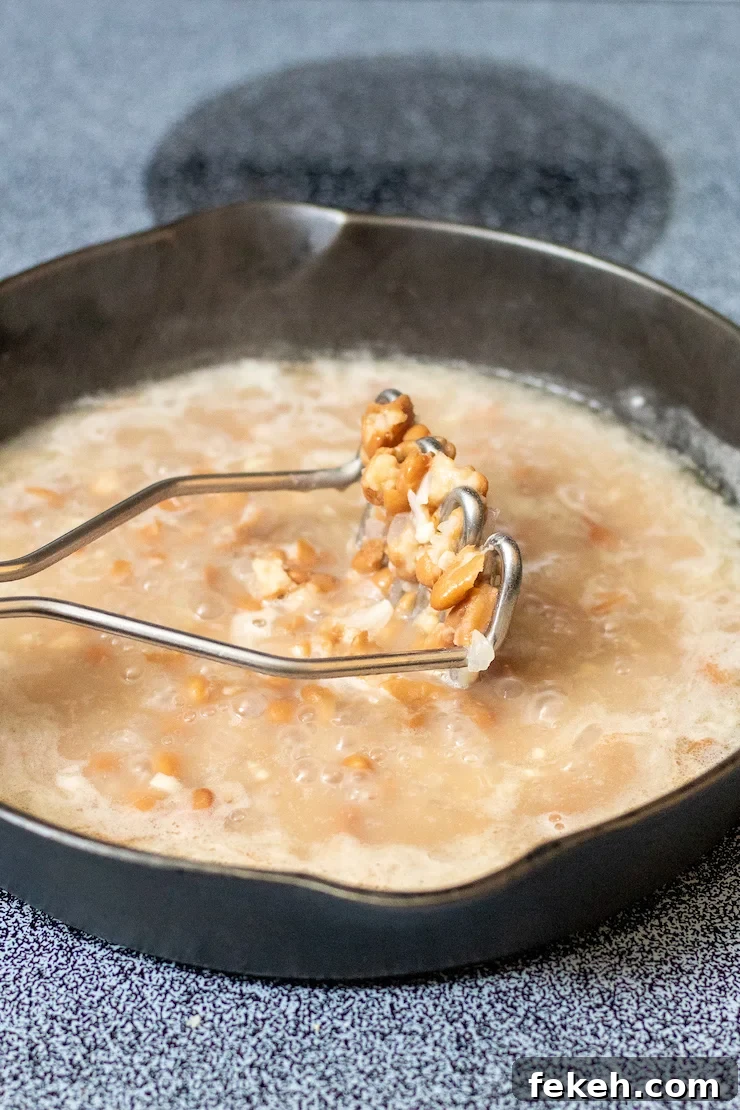 Homestyle Refried Beans Recipe for Creamy, Flavorful Sides 4 Potato masher in skillet with beans mixture.