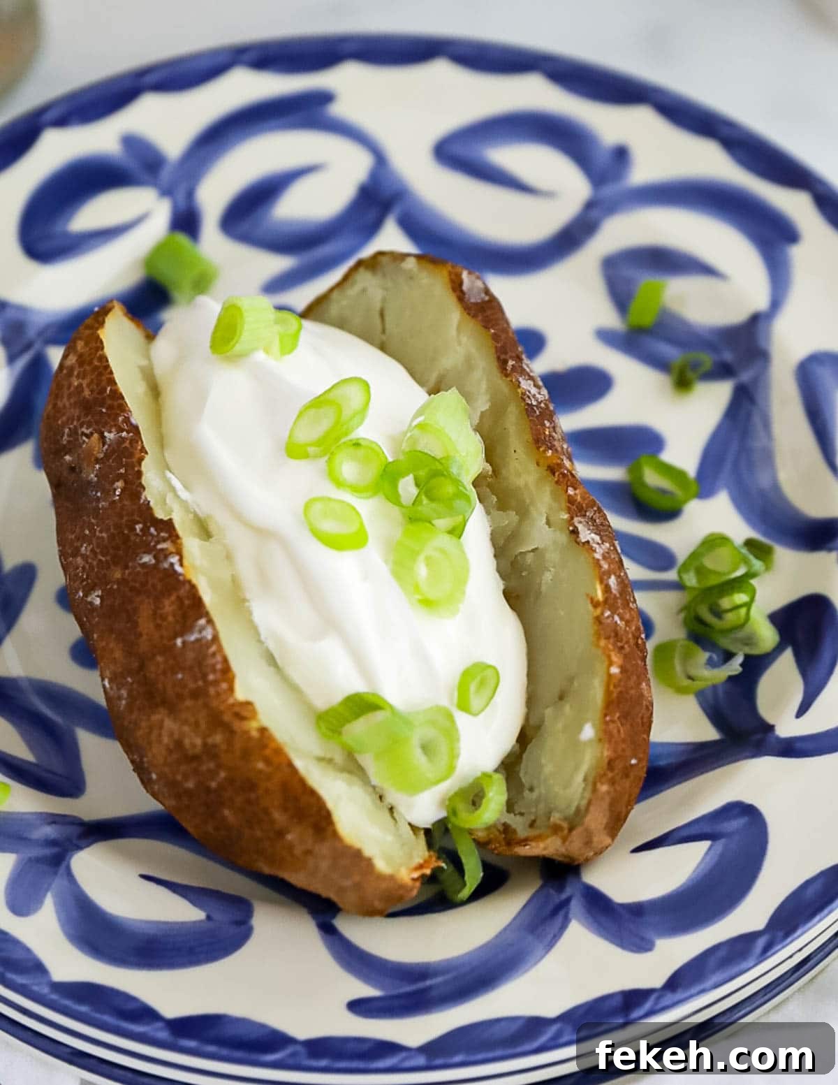 Crispy Air Fryer Baked Potatoes: Quick, Fluffy Centers 2 A sliced russet potato with a scoop of sour cream and sliced green onions in the potato.