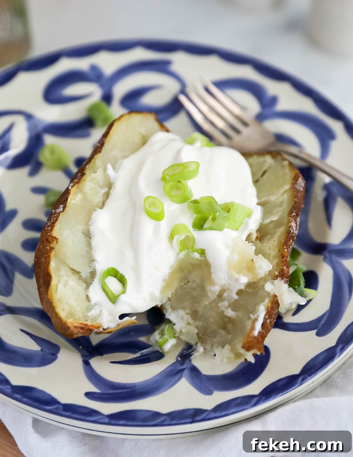 Crispy Air Fryer Baked Potatoes: Quick, Fluffy Centers 6 A baked potato on a blue and white plate with sour cream and sliced scallions.