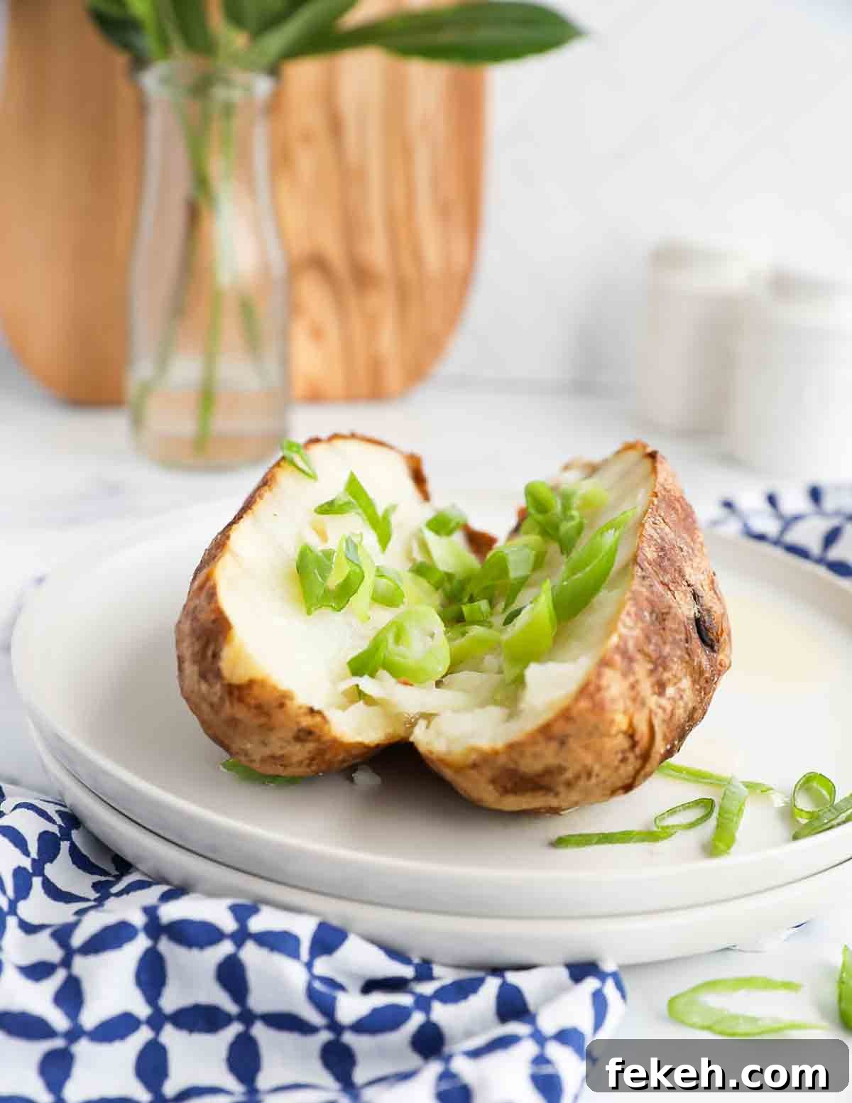Crispy Air Fryer Baked Potatoes: Quick, Fluffy Centers 7 A sliced baked potato covered in sliced green onions on two stacked white plates.
