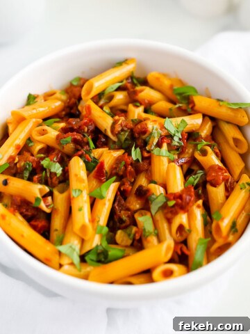 A white bowl filled with penne covered in a red sauce and topped with fresh green basil