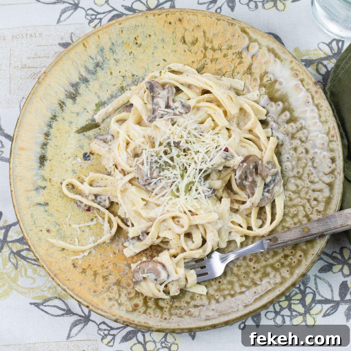 Mushroom Alfredo with milk served over cooked fettucinne noodles on a brown clay dinner plate.