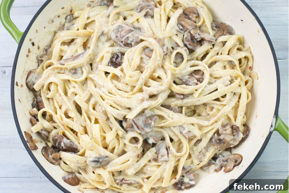 Closeup image of a skillet filled with creamy mushroom alfredo sauce with fettucine noodles.