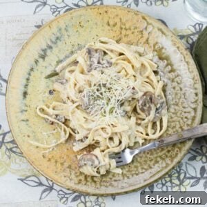 Mushroom Alfredo with milk served over cooked fettucinne noodles on a brown clay dinner plate.