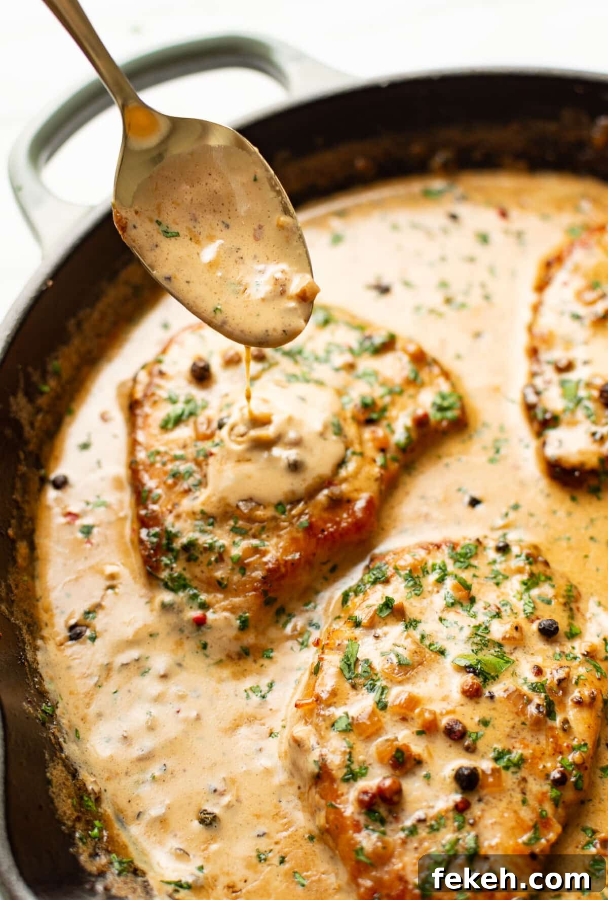 Creamy Peppercorn Sauce Pork Chops with Pan-Gravy 7 spooning peppercorn brandy sauce over a skillet with pork chops
