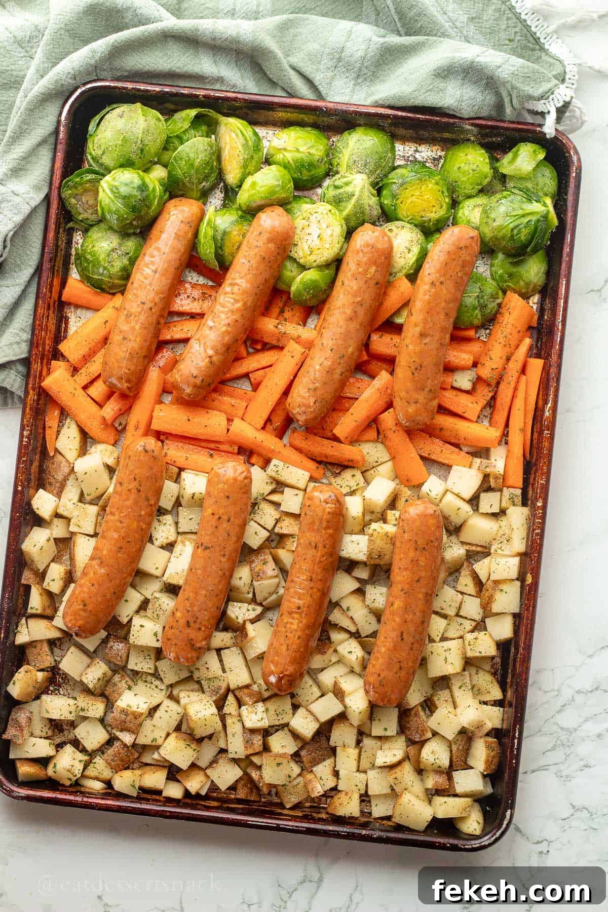 Sheet Pan Chicken Sausage with Roasted Veggies and Potatoes 8 Raw chicken sausage on top of potatoes, brussels sprouts, and carrots on metal pan.