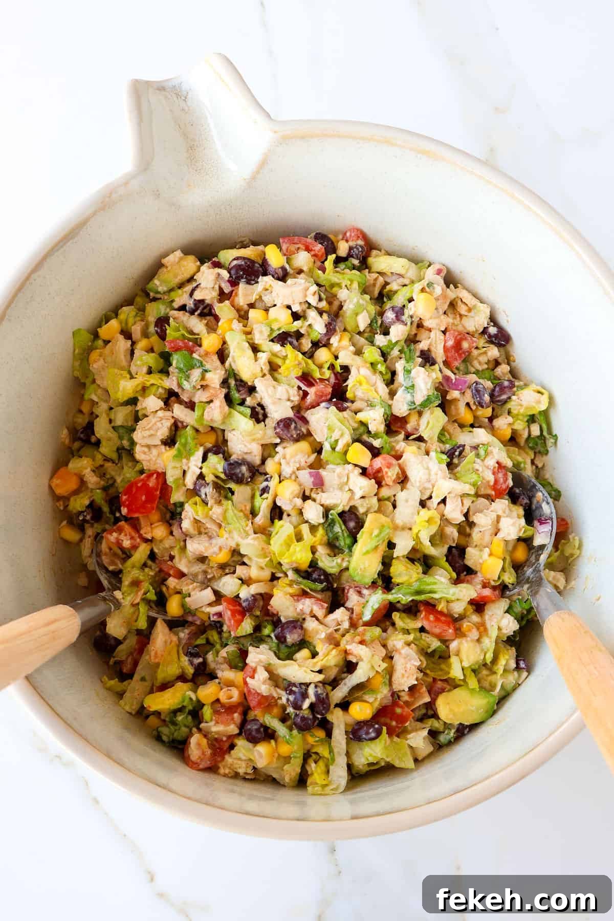 Crispy Chicken Salad Tostadas with Avocado and Lime 7 Tacos chicken salad in a mixing bowl with spoons.