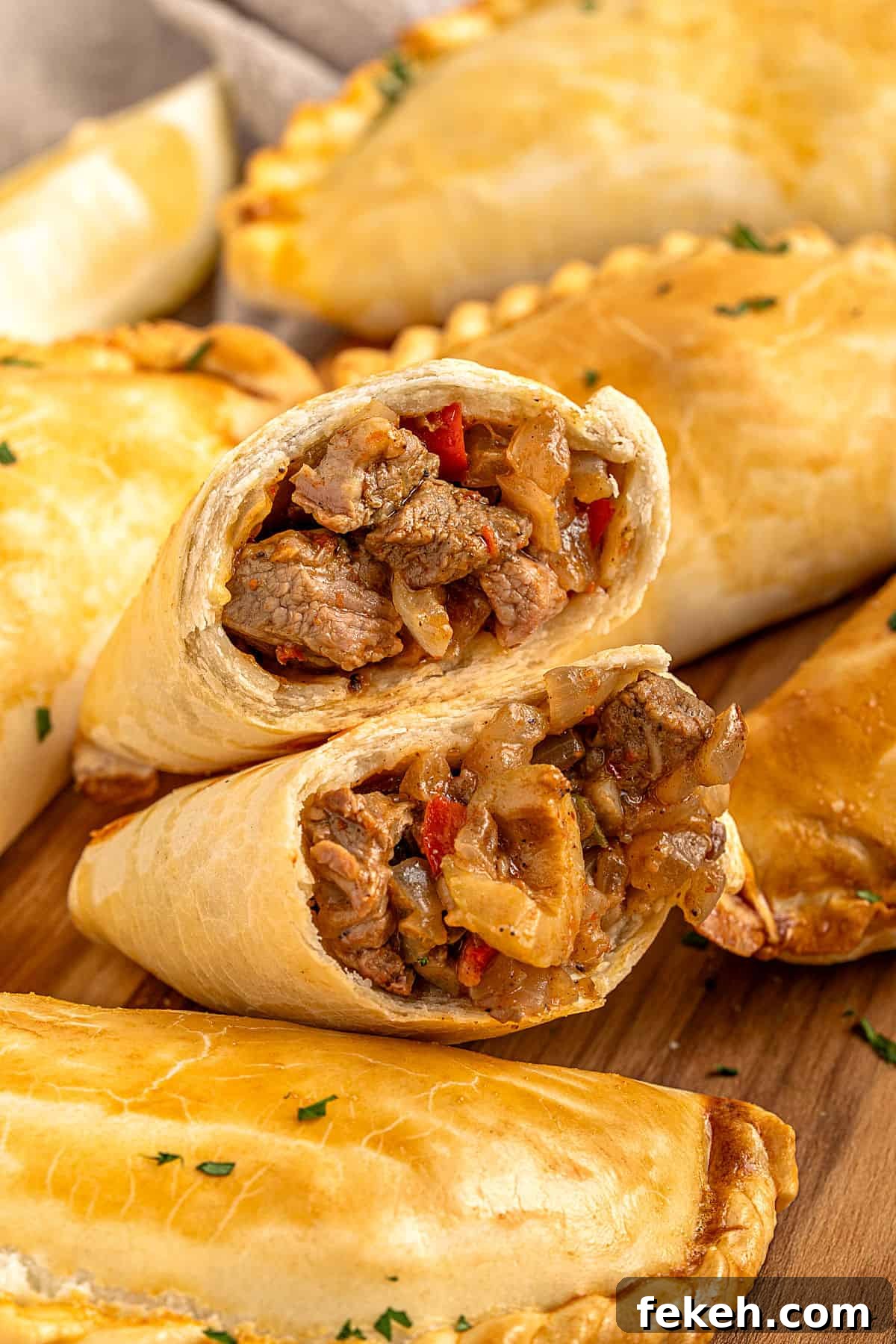 Knife-Cut Beef Empanadas: Crispy Handheld Meat Pastries 11 Knife-cut meat empanada halved with several whole ones. Wooden surface.