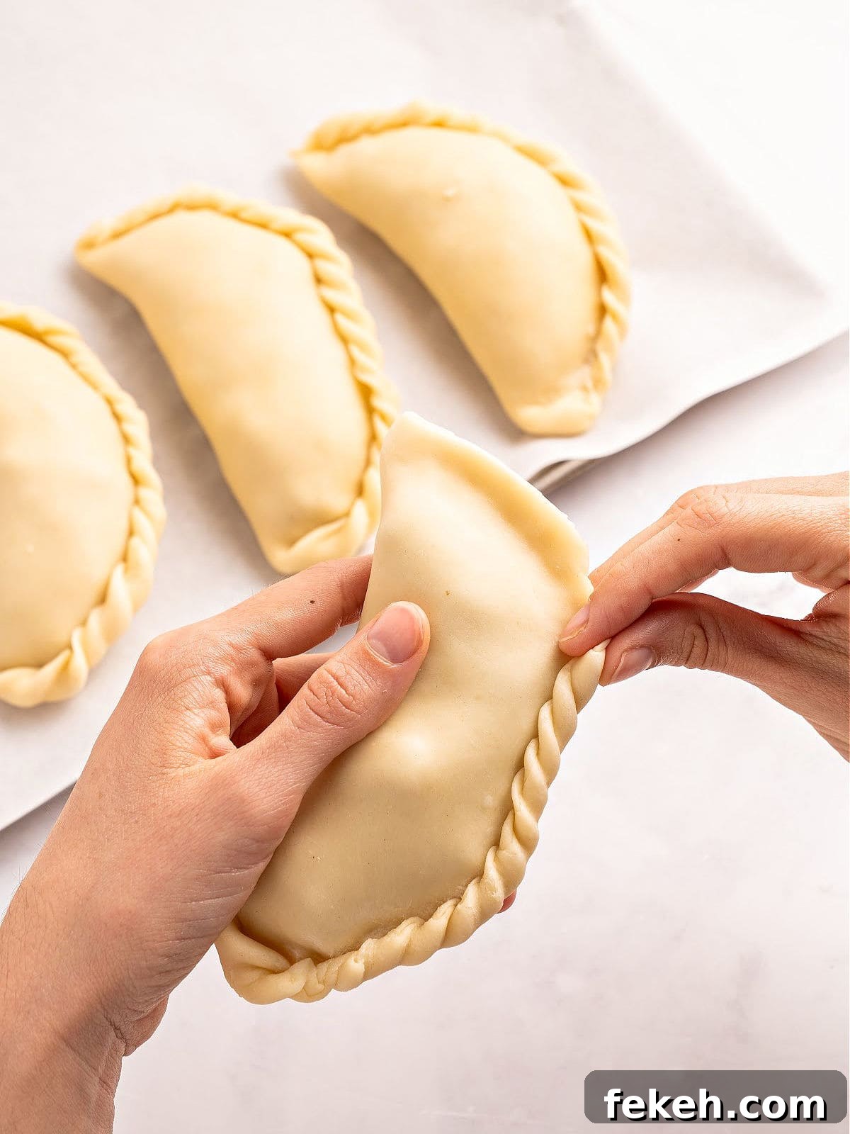 Knife-Cut Beef Empanadas: Crispy Handheld Meat Pastries 8 Crimping beef empanadas on a white surface.