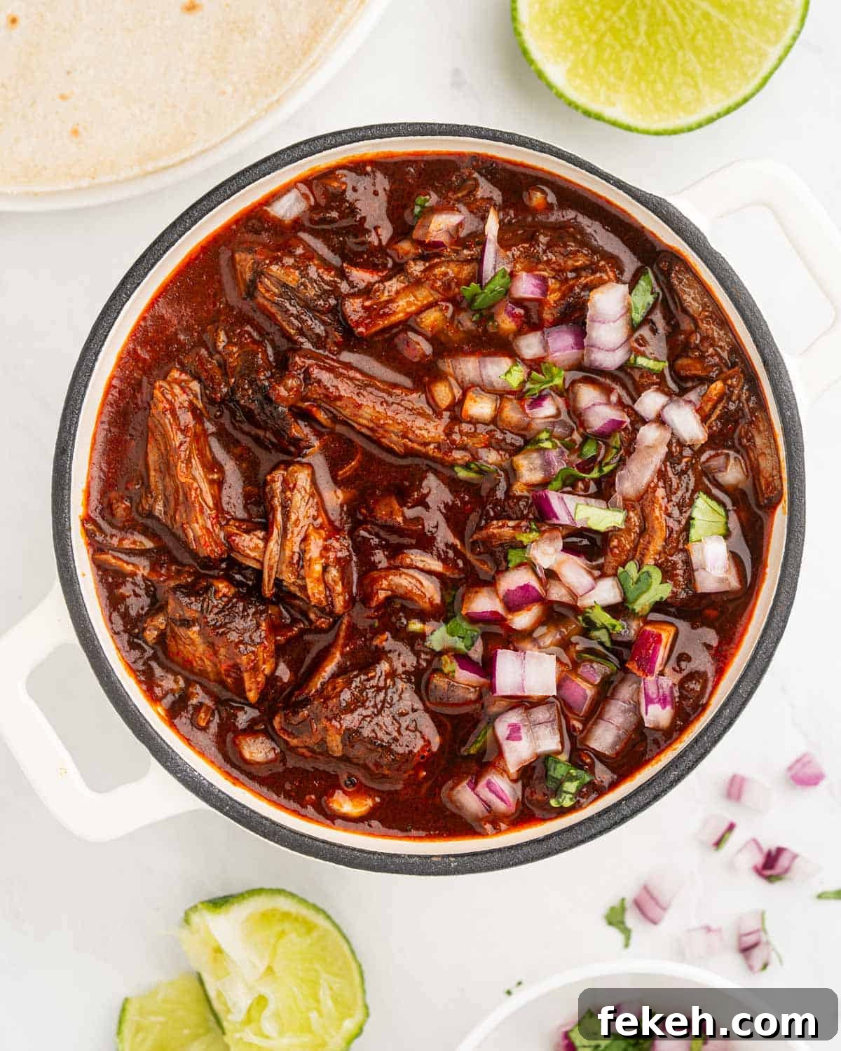 Authentic Quesabirria Tacos: How to Make Birria Tacos at Home 12 Shredded beef birria in a pot with sauce topped with diced onions and chopped cilantro.