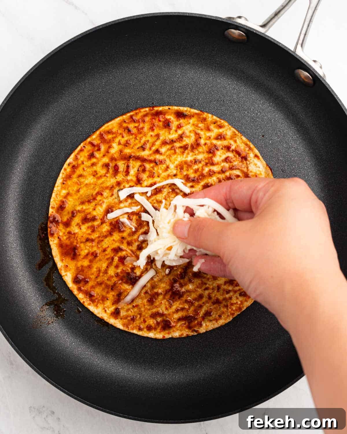 Authentic Quesabirria Tacos: How to Make Birria Tacos at Home 15 Hand spreading cheese on top of corn tortilla on a pan.