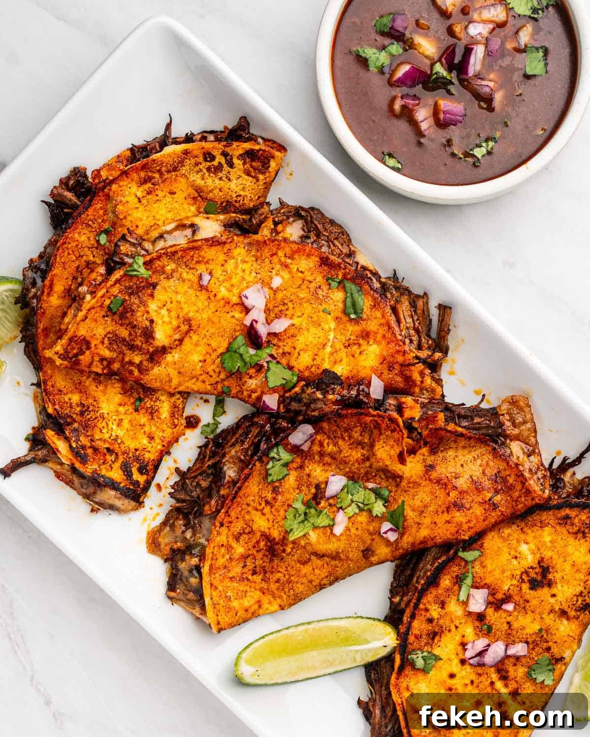 Authentic Quesabirria Tacos: How to Make Birria Tacos at Home 17 top down of birria tacos on a plate with side of lime and dipping sauce.