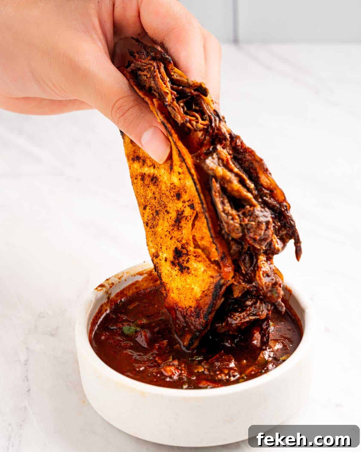 Authentic Quesabirria Tacos: How to Make Birria Tacos at Home 19 hand dipping birria taco into consommé sauce.