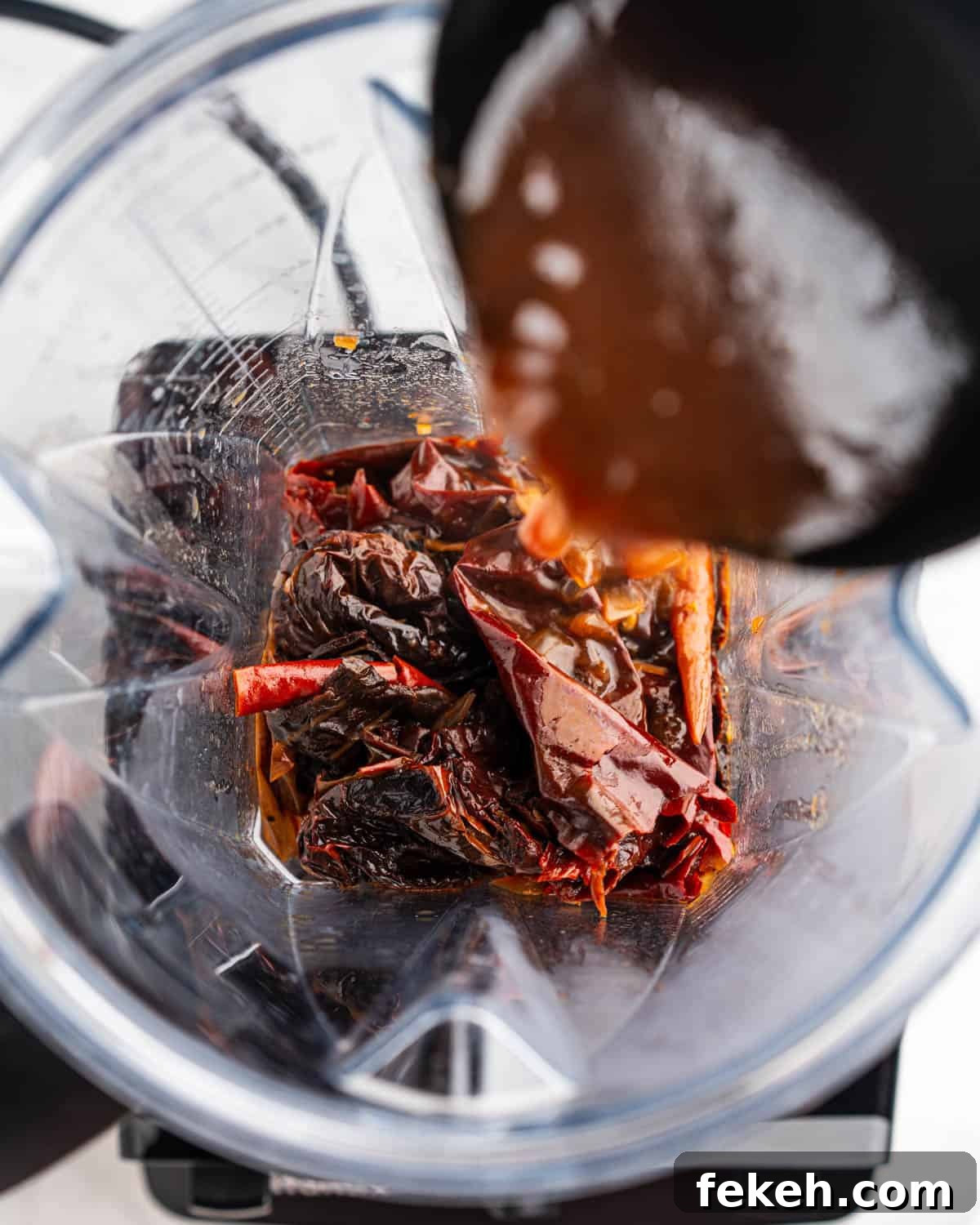 Authentic Quesabirria Tacos: How to Make Birria Tacos at Home 9 Cooked chili peppers in a blender with ladle adding broth.