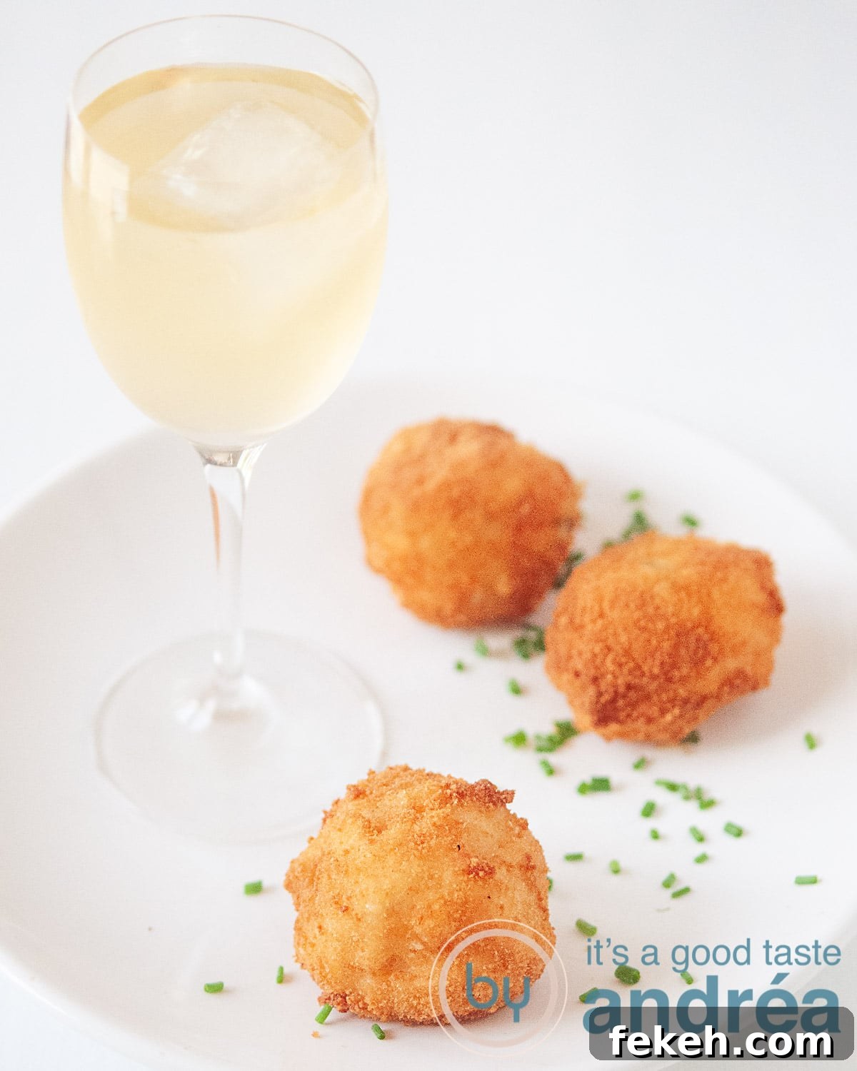 Three shrimp bitterballen on a white plate, sprinkled with chives. A glass of white wine to accompany the dish