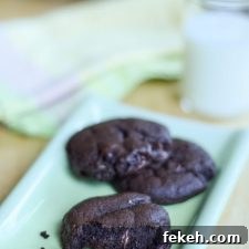 Dark chocolate cookies on a green rectangle plate with milk and more cookies in the background