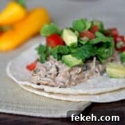 2 corn tortillas with chicken, lettuce, tomato and avocado on a tabletop