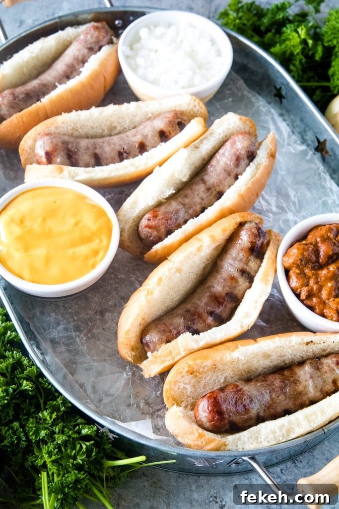 Spicy Chili Cheese Bratwurst Sandwiches for Game Day 5 Brats in buns on silver serving tray with toppings next to them.
