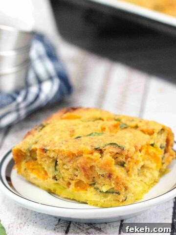 Egg casserole on a white plate with more casserole in a pan behind it and a blue linen with steel bowls on top beside it.