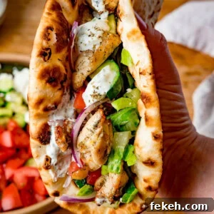 Grilled Chicken Souvlaki Recipe: Tender Mediterranean Skewers 7 A hand holds a toasted flatbread filled with chicken souvlaki, lettuce, tomato, cucumber, red onion, and homemade tzatziki sauce.