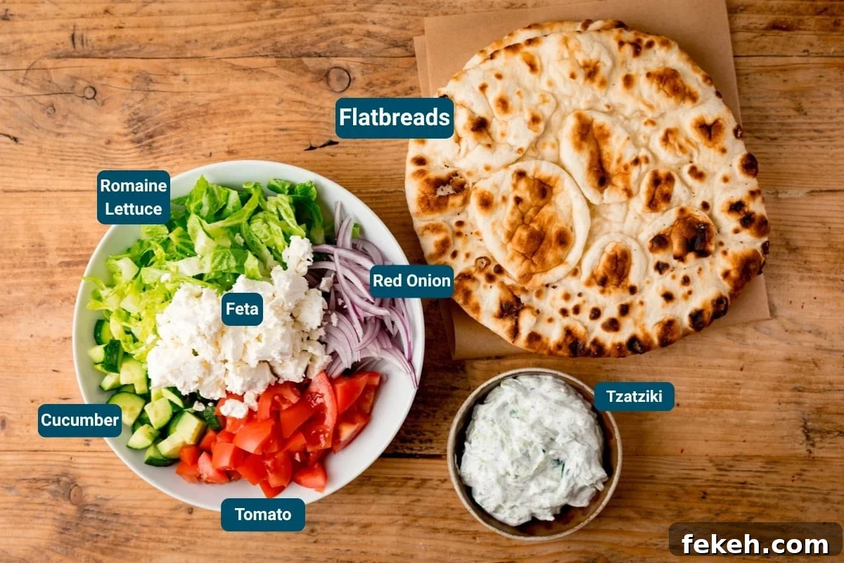 Grilled Chicken Souvlaki Recipe: Tender Mediterranean Skewers 5 A bowl with chopped lettuce, cucumber, tomato, feta, and red onion on a wooden table, next to flatbreads and homemade tzatziki. Ingredients are labelled.
