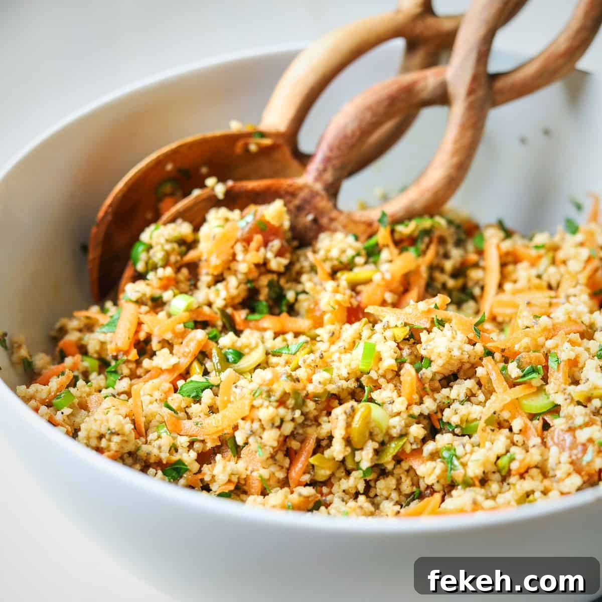 Square photo of a white serving bowl filled with spiced millet salad with two serving spoons.