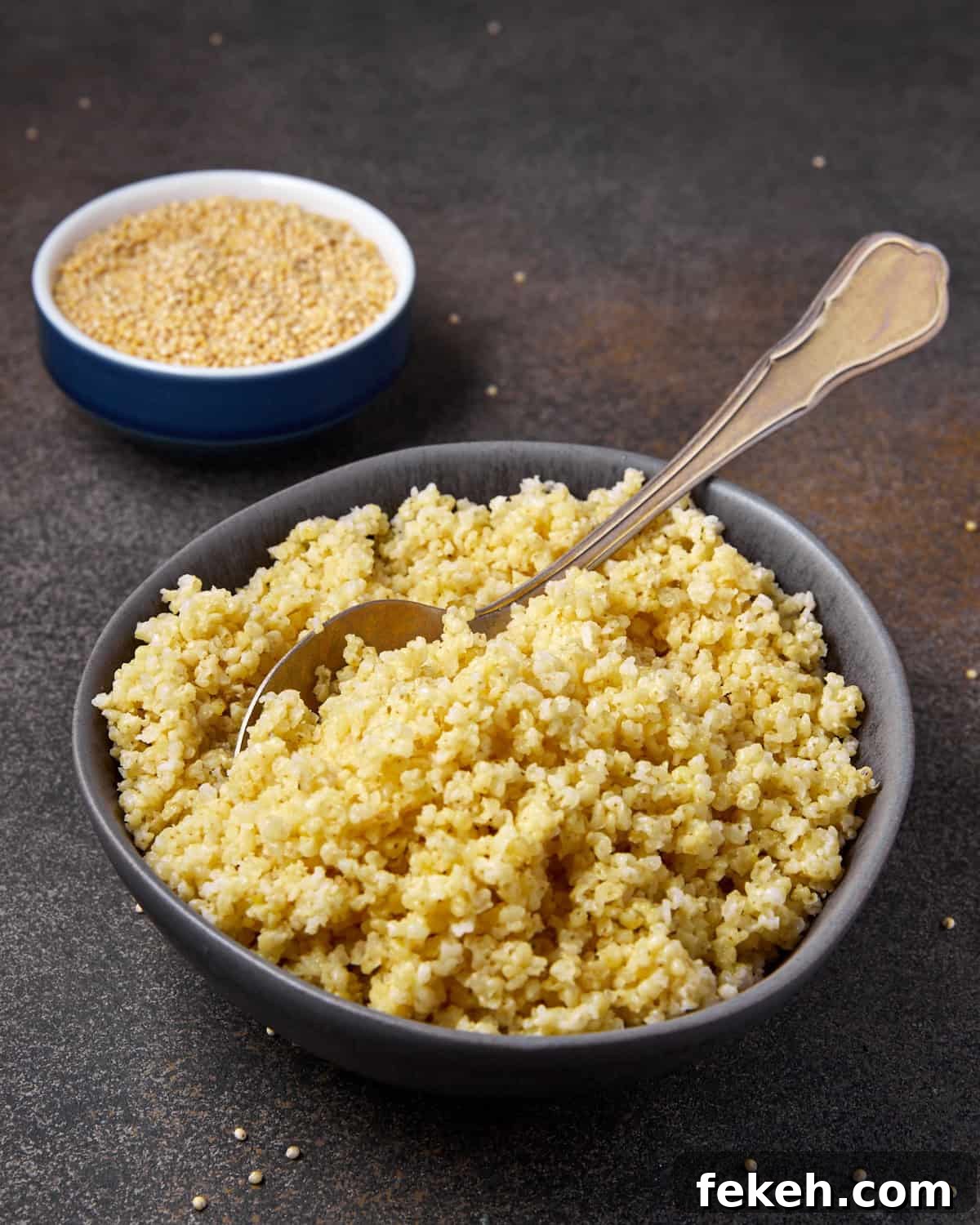 How to Cook Millet Perfectly on Stovetop or Instant Pot 3 Photo showing a bowl of cooked millet with a spoon and a smaller bowl of raw millet seeds in the background.