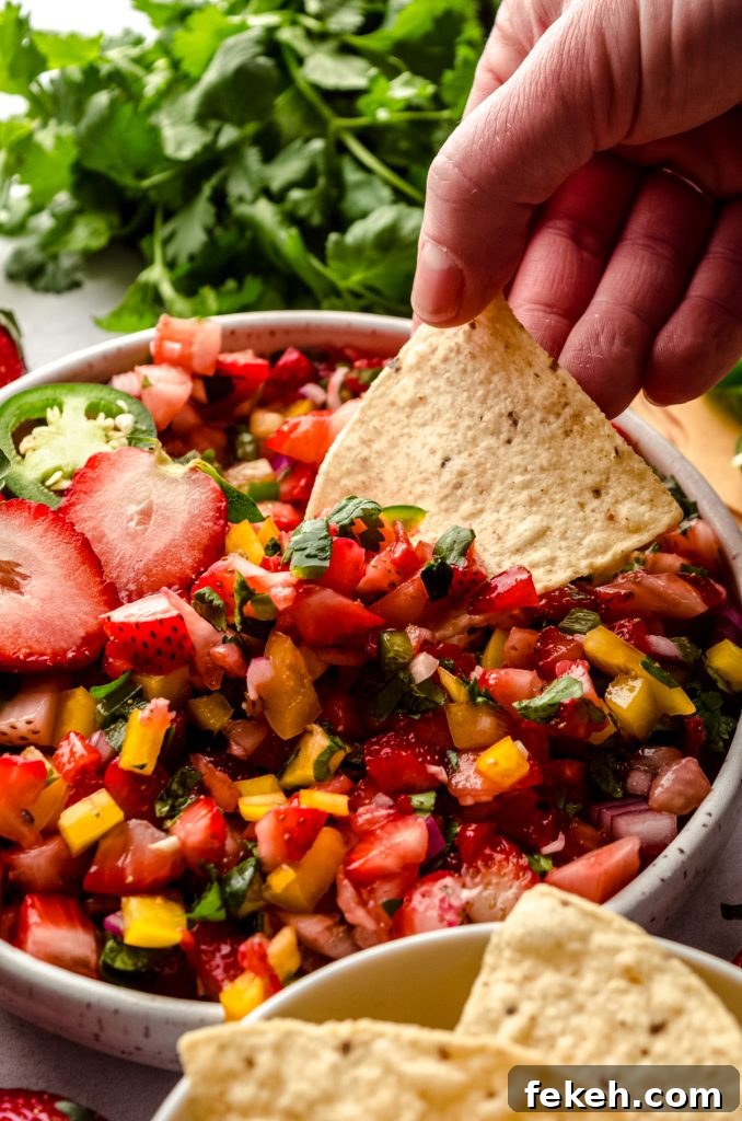 Fresh Strawberry Salsa Recipe: Zesty Fruit Salsa for Chips & Tacos 13 Someone is dipping a tortilla chip into a bowl of fresh strawberry salsa.