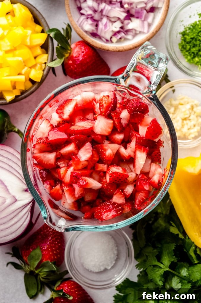 Fresh Strawberry Salsa Recipe: Zesty Fruit Salsa for Chips & Tacos 7 A measuring cup of chopped strawberries surrounded by other salsa ingredients like a red onion, yellow pepper, cilantro, and a lime.