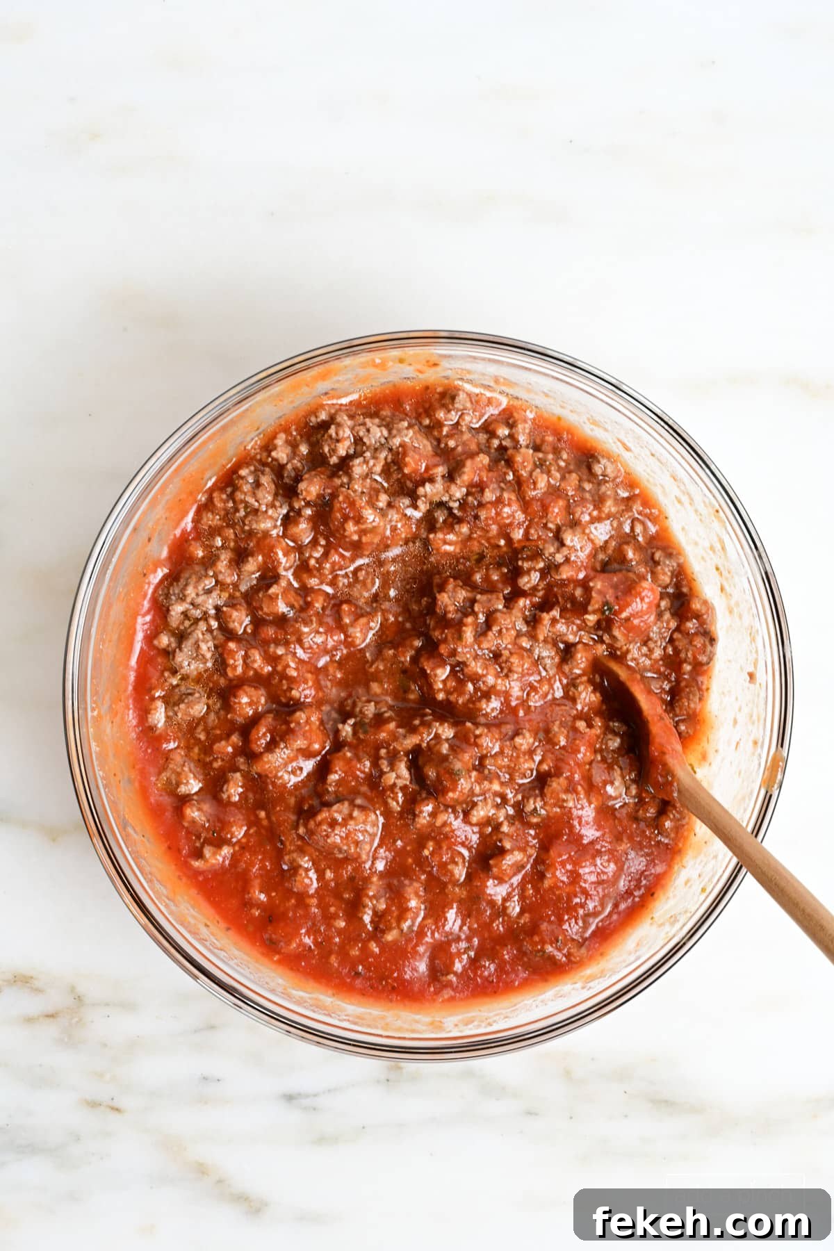Cheesy Baked Spaghetti Casserole Recipe for Weeknight Dinners 4 Marinara Sauce in a glass mixing bowl with a wooden spoon.