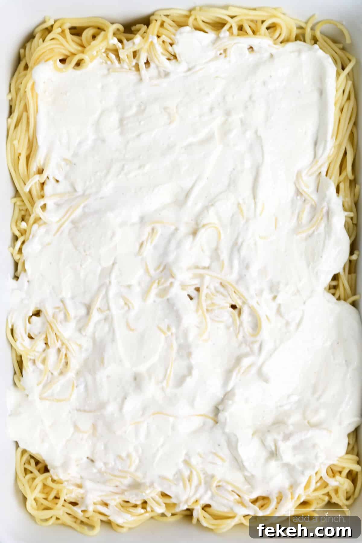 Cheesy Baked Spaghetti Casserole Recipe for Weeknight Dinners 8 Cooked spaghetti and cheese layer in a baking dish.