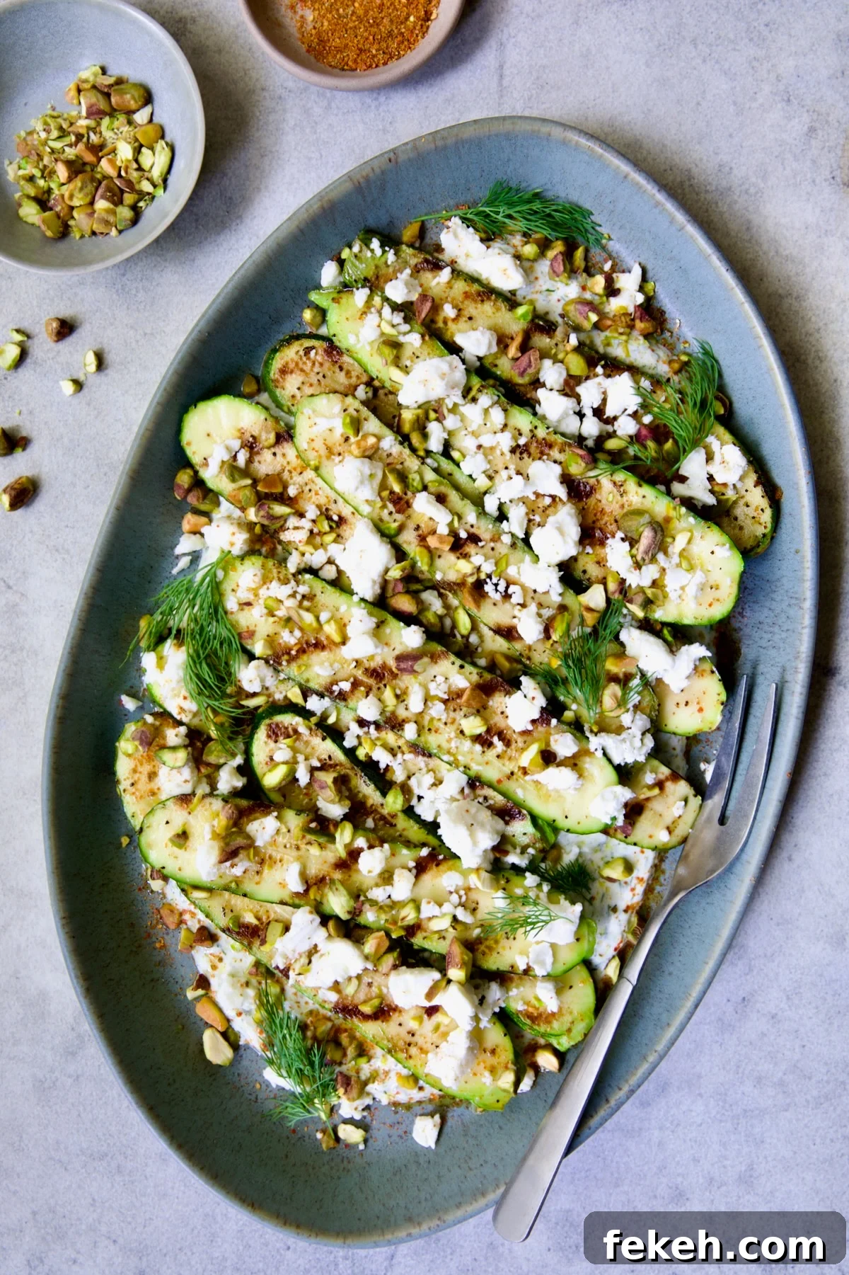 Mediterranean Grilled Zucchini with Dill Yogurt & Feta 2 Mediterranean Grilled Zucchini with Dill Yogurt and Feta on blue platter garnished with pistachios and fresh dill sprigs.