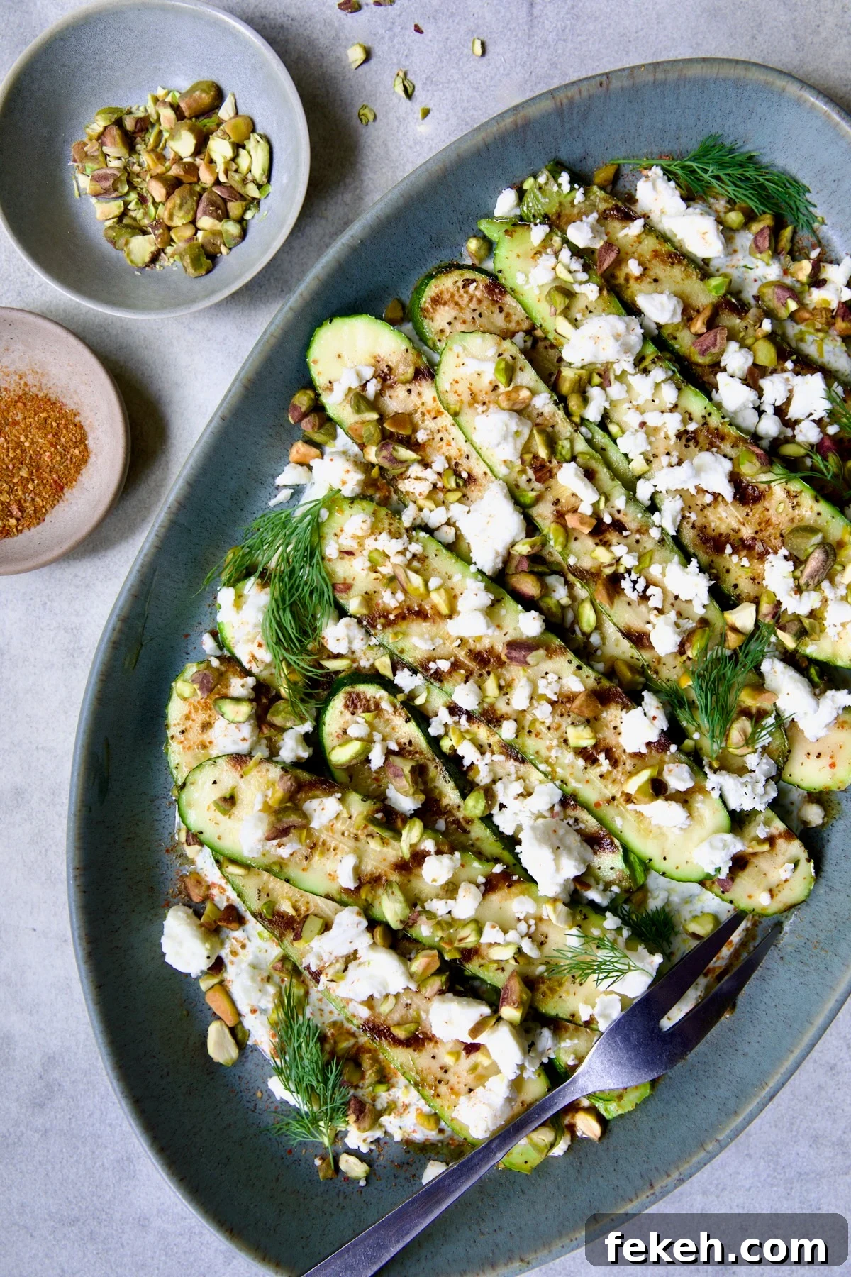 Mediterranean Grilled Zucchini with Dill Yogurt & Feta 12 Mediterranean Grilled Zucchini with Dill Yogurt and Feta on blue platter garnished with pistachios and fresh dill sprigs.