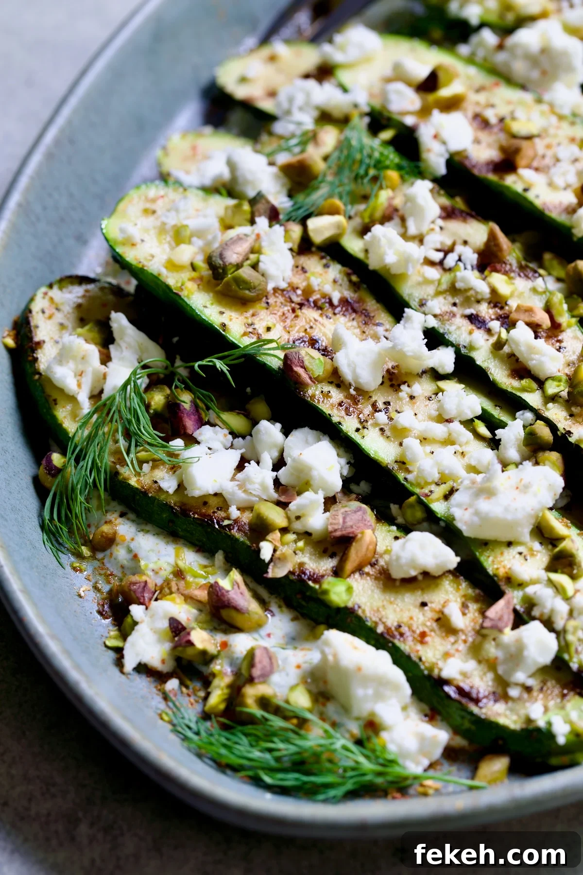 Mediterranean Grilled Zucchini with Dill Yogurt & Feta 3 Mediterranean Grilled Zucchini with Dill Yogurt and Feta on blue platter garnished with pistachios and fresh dill sprigs.