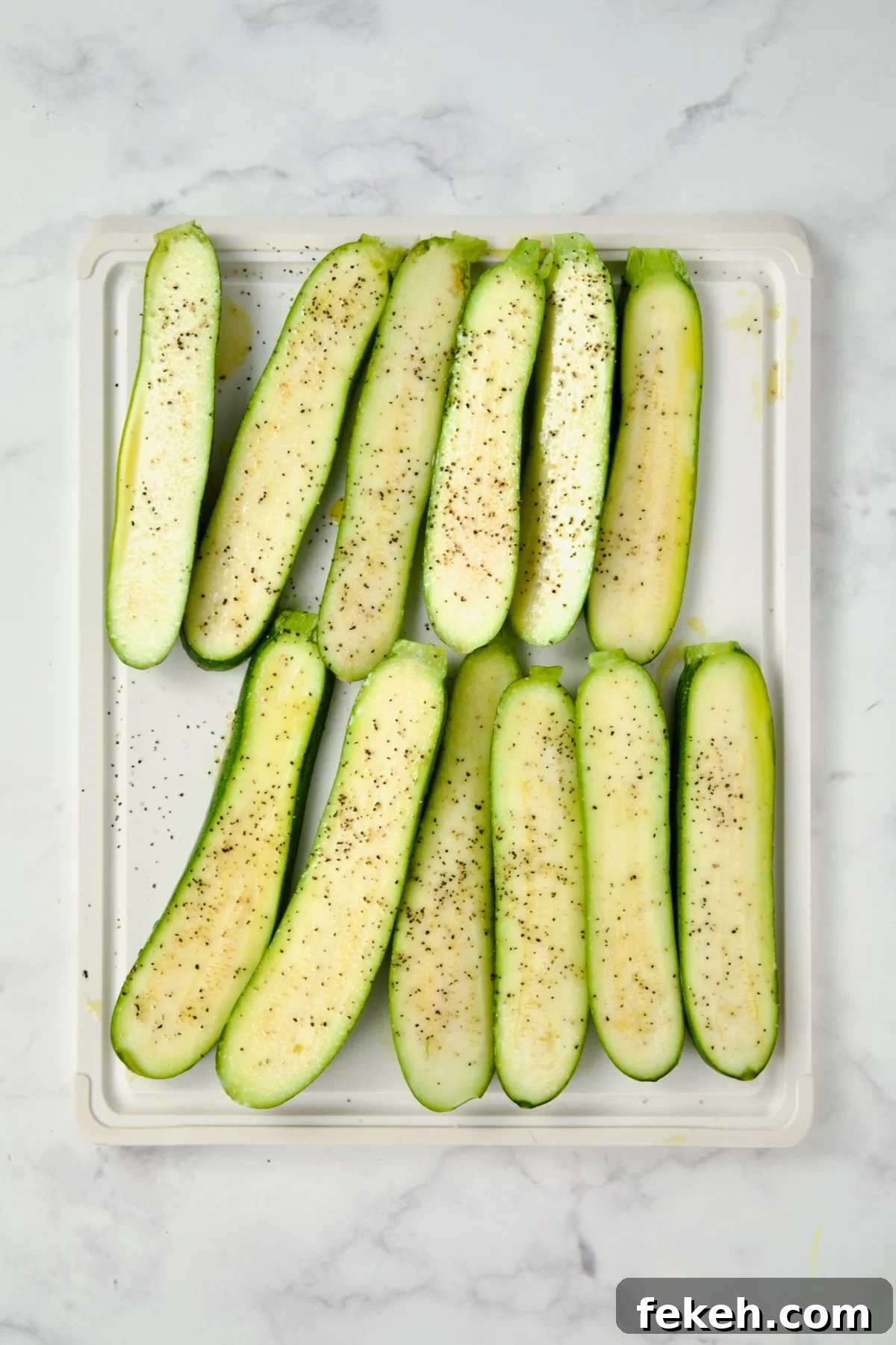 Mediterranean Grilled Zucchini with Dill Yogurt & Feta 7 Sliced zucchini on white plastic cutting board seasoned with salt, pepper and drizzled with olive oil.