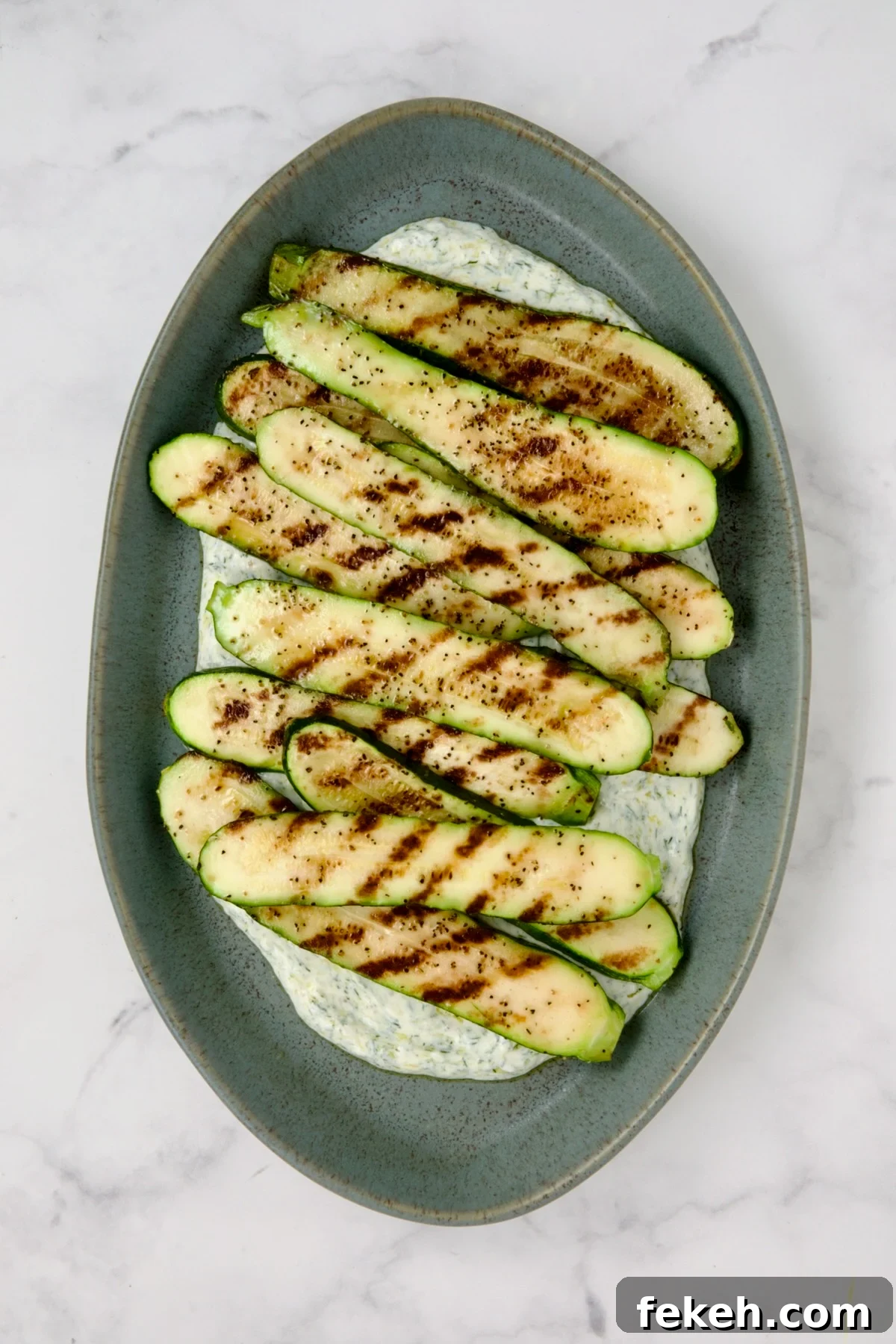 Mediterranean Grilled Zucchini with Dill Yogurt & Feta 10 Grilled zucchini slices placed over dill yogurt on blue platter.