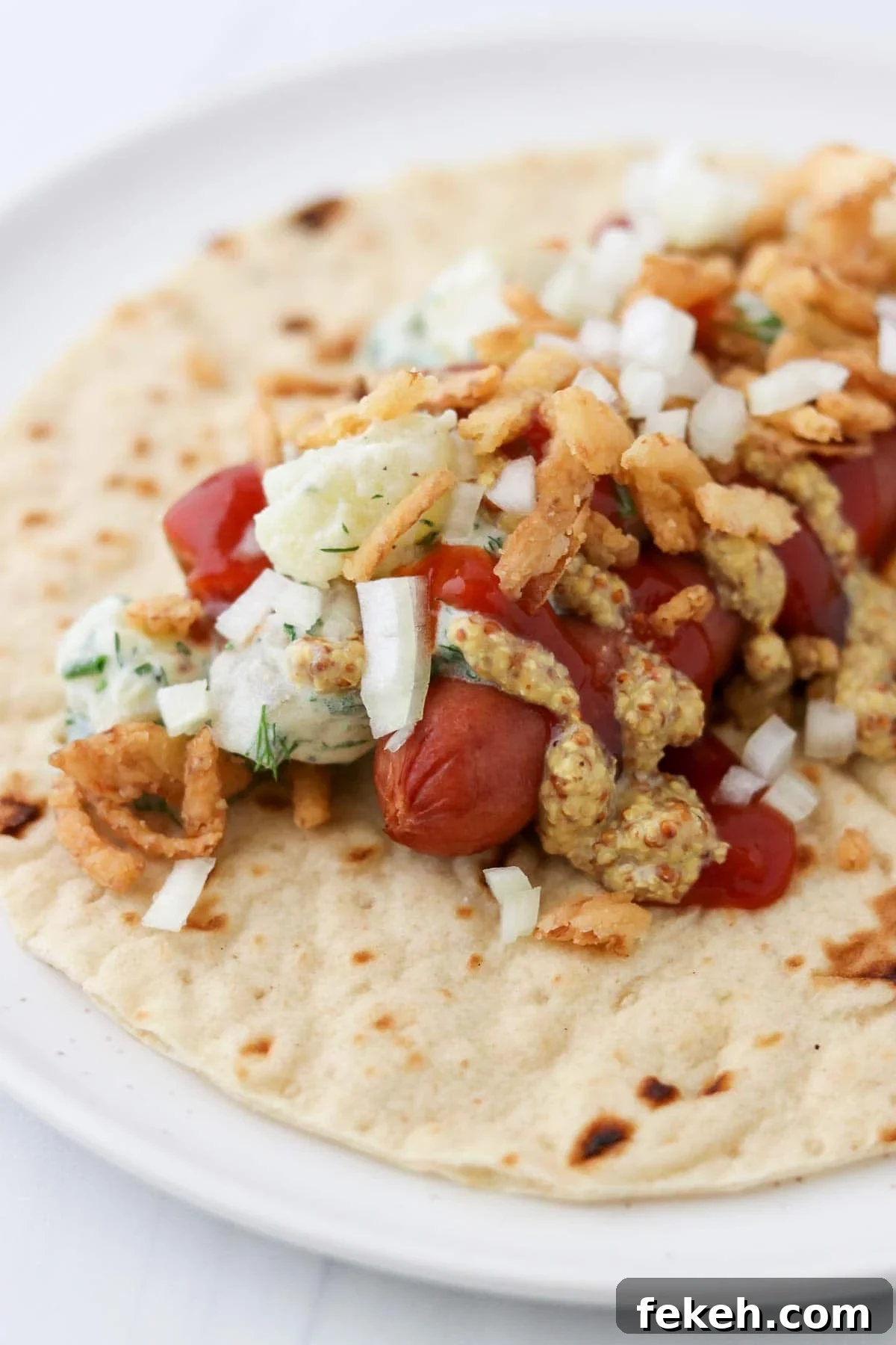 Hot dog on top of a tortilla topped with potato salad, onions, mustard and ketchup.